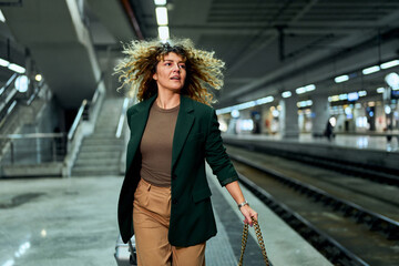In a rush at the subway station, a curly-haired woman in her 30s dashes with a travel suitcase,...