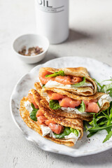Yummy crepes or thin pancakes with smoked salmon, soft cheese and spinach on a plate close up on gray textured background. Pancake day, Maslenitsa