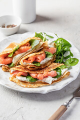 Yummy crepes or thin pancakes with smoked salmon, soft cheese and spinach on a plate close up on...