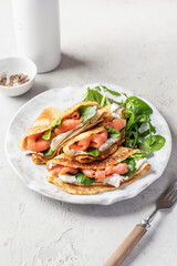 Yummy crepes or thin pancakes with smoked salmon, soft cheese and spinach on a plate on gray textured background. Pancake day, Maslenitsa