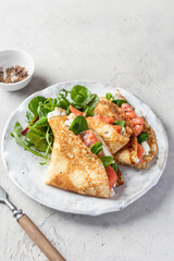 Crepes or thin pancakes with smoked salmon, soft cheese and spinach on a plate on gray textured background. Pancake day, Maslenitsa, text space