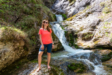 Naklejka premium Hiker woman next to idyllic river Foelzbach, Hochschwab mountains, Styria, Austria. Hiking trail in alpine forest. Remote Austrian Alps in summer. Sense of escapism, reflection. Connect with nature
