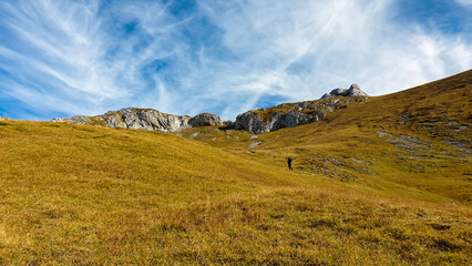 Hiker man on golden alpine meadow with scenic view of Hochschwab mountain range, Styria, Austria. Hiking trail in alpine terrain. Remote Austrian Alps in summer. Escapism. Connect with nature