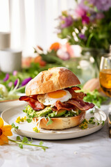 Bacon and egg breakfast sandwich in a white kitchen on the table with a runny yolk - 735398845