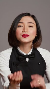 Vertical Video Cute flirty waitress blowing air kisses in front of camera, acting romantic with sweet gesture. Asian restaurant employee posing with a kissy facial expression, catering industry