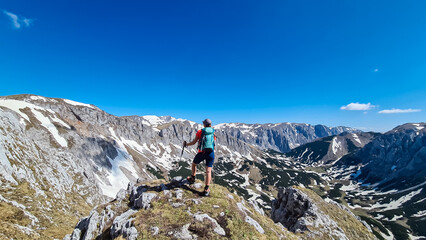 Naklejka premium Hiker woman with panoramic view of majestic mountain peak Ringkamp in wild Hochschwab massif, Styria, Austria. Scenic hiking trail in remote Austrian Alps on sunny day. Wanderlust in alpine spring