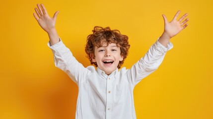 Happy boy in white shirt smiling and raising arms while looking at camera on yellow background