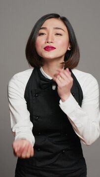 Vertical Video Cute flirty waitress blowing air kisses in front of camera, acting romantic with sweet gesture. Asian restaurant employee posing with a kissy facial expression, catering industry