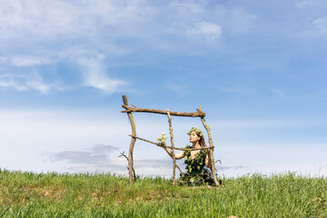 Young beautiful girl wearing dress with white flowers and spring branches in her hair, cheerful lady on the grass in nature. Copy the field.