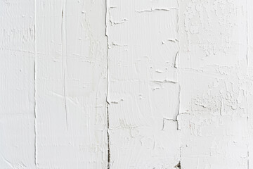 A close-up of a white painted wall with varying textures, showing smooth areas, brush marks, and cracking paint.