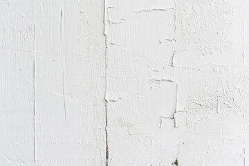 Fototapeta premium A close-up of a white painted wall with varying textures, showing smooth areas, brush marks, and cracking paint.