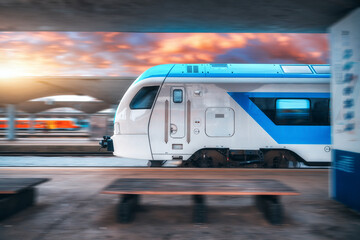 Blue high speed train in motion on the railway station at sunset