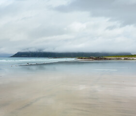 Summer misty and cloudy beach view with white sand and sky reflections in Ramberg (Norway, Lofoten).