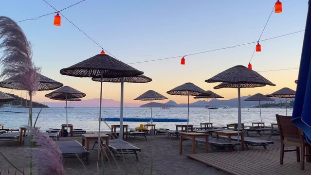 Beach umbrellas and loungers under red lanterns against backdrop of the sea at sunset. Summer vacation concept