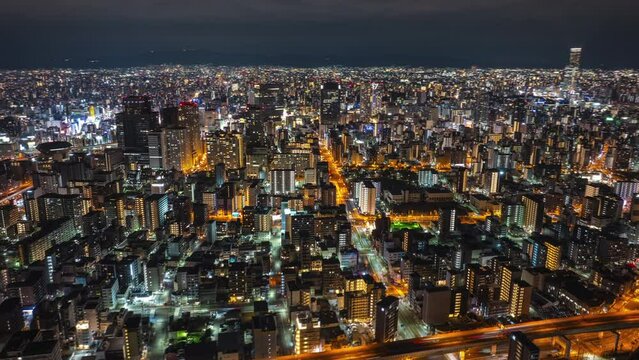 Amazing aerial panoramic shot of metropolis in evening. Busy roads and illuminated high rise buildings in urban boroughs. Night hyper lapse. Osaka, Japan