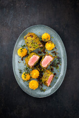 Fried mangalica pork tenderloin coated with crashed pistachio nuts, grated parmesan and chopped cranberries offered with princess potatoes as top view on a Nordic design plate