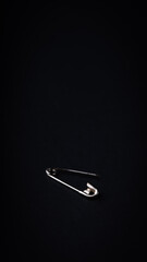 A safety pin against a black backdrop with space for text, captured from an overhead perspective.