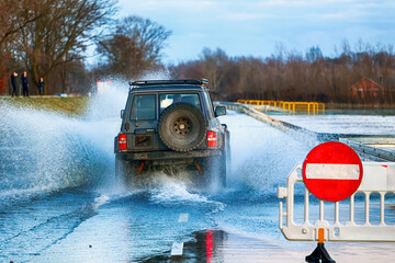Samochody na zalanej drodze przez wodę z rzeki. Powódź.  - obrazy, fototapety, plakaty
