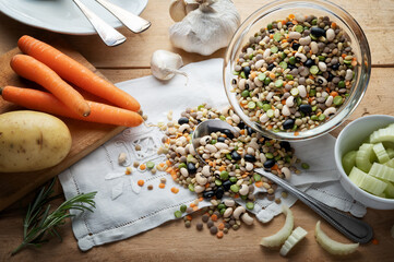 Ingredients for legume and cereal soup with carrots, celery, potatoes, rosemary and garlic on wooden background, close-up.