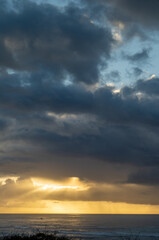 Sunset View of Diamond Head Beach with Gold and Gray Clouds and Sunlight in a Rain Shower.