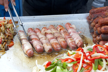 Street vendor cooking bacon wrapped hot dogs, tongs turning food. Popular cuisine for street fairs and events