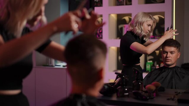 Young female hairdresser concentrates on doing a mans haircut while standing in a modern hairdressing salon. Slow motion