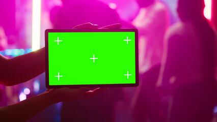 Fototapeta na wymiar Person showing tablet with greenscreen at nightclub, being on the dance floor holding device with mockup template. Girl looking at isolated chroma key display with blank copyspace.
