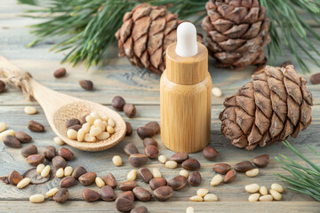 Cedar essential oil bottle, whole and shelled nuts on bamboo spoon, pine cones and green needle branches on wooden table. Cedar nuts products for nutrition and spa body relaxation.
