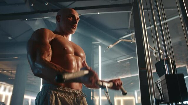 A muscular man with a bare torso engages in a bicep curl exercise at a cable machine, demonstrating his impressive physique and commitment to fitness. Camera 8K RAW.