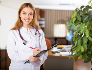 Doctor woman in white gown and stethoscope on sholders standing in hall of clinic and holding...