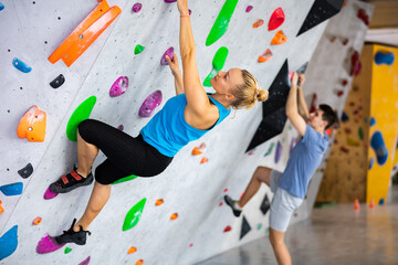 Caucasian woman exercising on wall in climbing gym during bouldering training. Young man climbing...