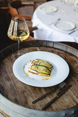 Appetizing ratatouille on a large white plate with a glass of white wine