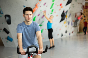 Young man riding exercise bike to warm-up before training in bouldering center.