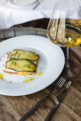 Appetizing ratatouille on a large white plate with a glass of white wine