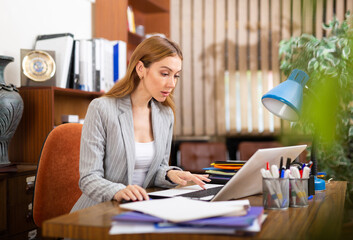 Young clerical worker sitting at desk in office and using laptop for work.