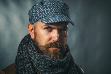 Men fashion. Closeup portrait of serious man with beard and mustache in cap and knitted scarf....