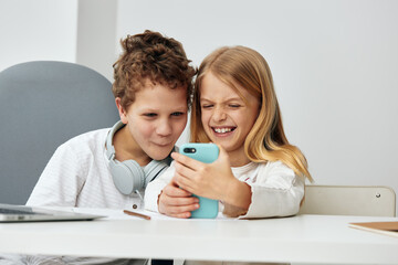 Happy Caucasian school children sitting at home on the living room table, engrossed in their laptops and tablets The boy and girl are engaged in online learning, wearing headphones and typing on their