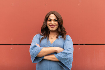 Portrait of happy trans woman with crossed-arms. Blue dress, red background. LGBT concept.