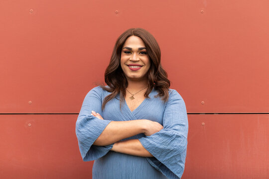 Portrait of happy trans woman with crossed-arms. Blue dress, red background. LGBT concept.