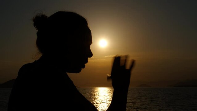 Female with asthma by sea. A tourist female silhouette with asthma attack use an inhaler on the beach during evening time.