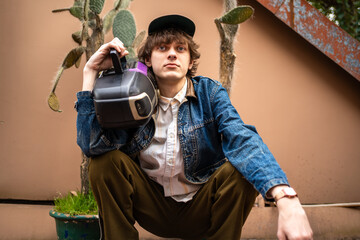 Young stylish male hipster wear in retro 90s old-fashioned style hold audio tape cassette recorder player.