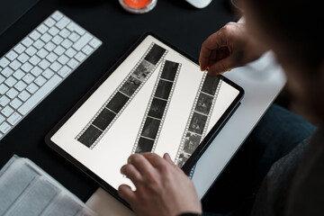 A photographer scrutinizes film negatives on a digital tablet, bridging traditional photography...