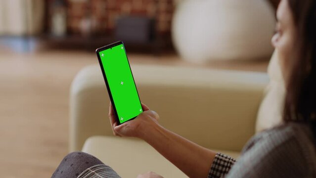 Woman using green screen smartphone gyroscope function while sitting on cozy couch at home. Person relaxing in apartment, turning chroma key mobile phone in landscape mode, close up shot