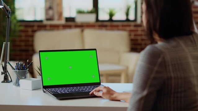 Freelancer checking emails on green screen laptop during work from home at computer desk. Self employed woman in cozy bright apartment doing job tasks, reading business messages on mockup device