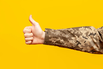 the hand of a Ukrainian soldier in a camouflage pixel uniform shows like and recommends on a yellow...