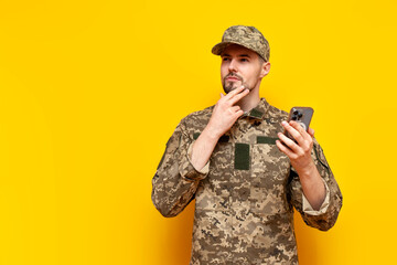 a thoughtful Ukrainian army soldier in a pixel camouflage uniform uses a smartphone and plans on a...
