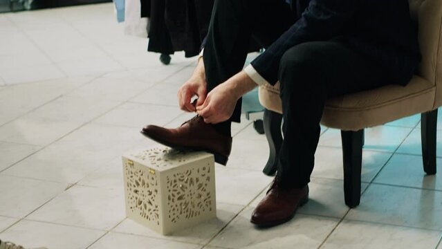 Elderly customer shopping for new shoes to match his elegant suit, trying on a pair of classy leather footwear with laces. Store employee making suggestions for regular client in showroom. Camera A.