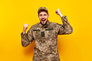 Ukrainian army soldier in pixel camouflage uniform celebrates victory and success on a yellow...