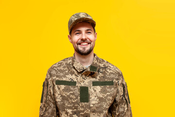Ukrainian army soldier in camouflage pixel uniform smiling on yellow isolated background, Ukrainian...