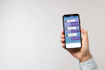 Man texting with friend using messaging application on smartphone against light grey background, closeup. Space for text